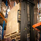Een heftruck tilt een houten pallet op die hoog is opgestapeld met kartonnen dozen in een distributiecentrum met stellingen